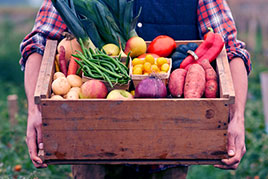 a man holding a wooden crate full of colorful vegetables