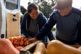 a man and woman handle crates of vegetables in a work van